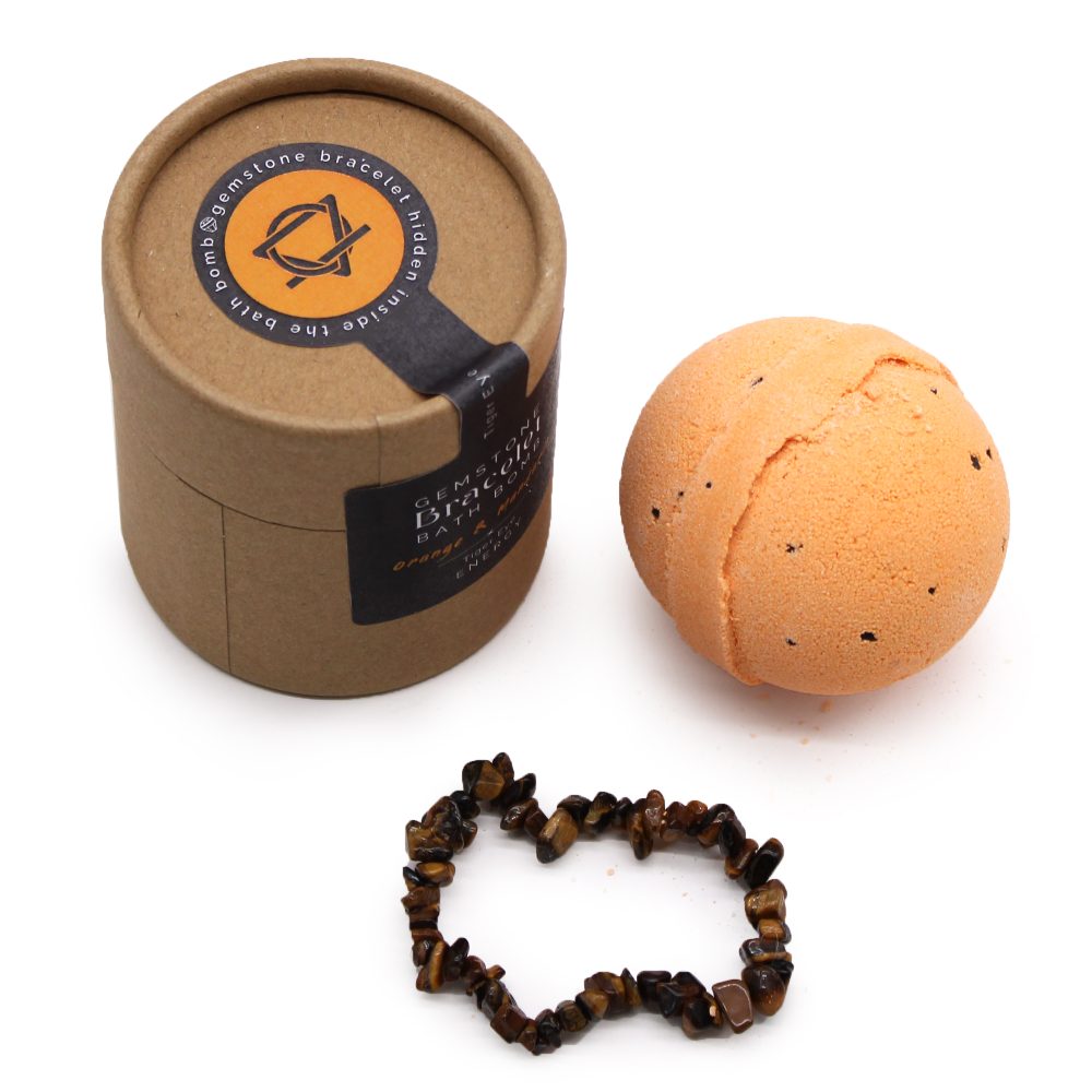 A round, orange bath bomb sits beside a brown cylindrical box labeled "Gemstone Diffuser Bath Bomb. Orange & Clove," with a gemstone bracelet nearby.