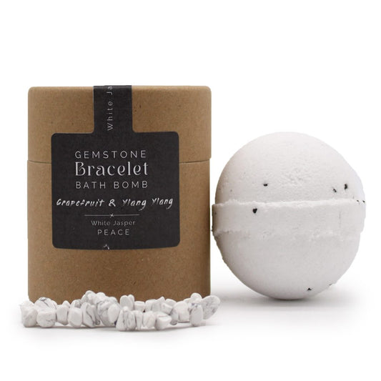 A cylindrical cardboard container labeled "Gemstone Bracelet Bath Bomb Grapefruit & Ylang Ylang x White Jasper PEACE" sits next to a white bath bomb. White jasper stones are scattered in front.