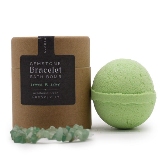A green bath bomb sits beside a cylindrical cardboard container labeled "GEMSTONE Bracelet BATH BOMB Lemon & Lime Aventurine Green PROSPERITY," with an aventurine gemstone bracelet resting nearby.