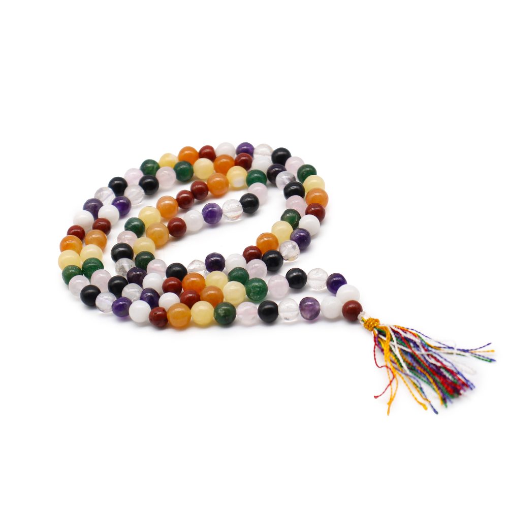 A mala, or set of prayer beads, is coiled and lies in a "Q" shape on a white surface. It is made from round beads in multiple colors and has a multicolored tassel.