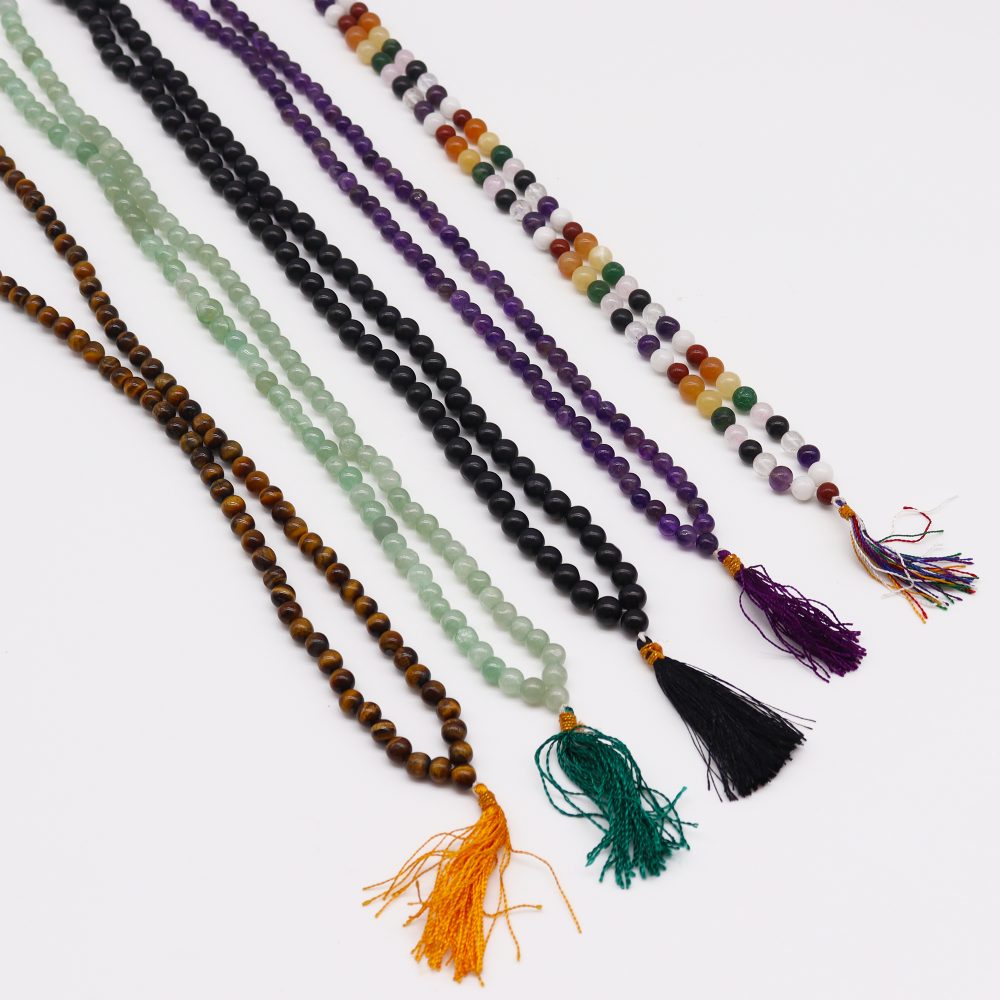 Six colorful beaded necklaces extend diagonally across a white background, each ending in a tassel of various colors.