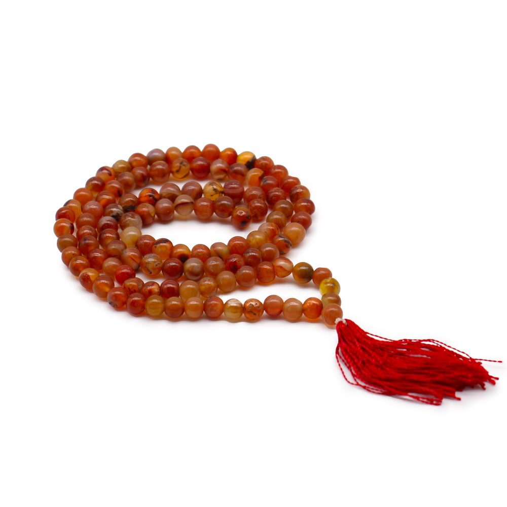 A string of orange and brown beads coils, with a red tassel hanging from one end, on a plain white surface.
