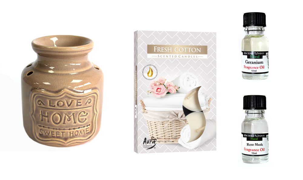 A ceramic oil burner, displaying "LOVE HOME SWEET HOME," diffuses fragrance oils; alongside are scented candles and two bottles of geranium and rose musk fragrance oil.