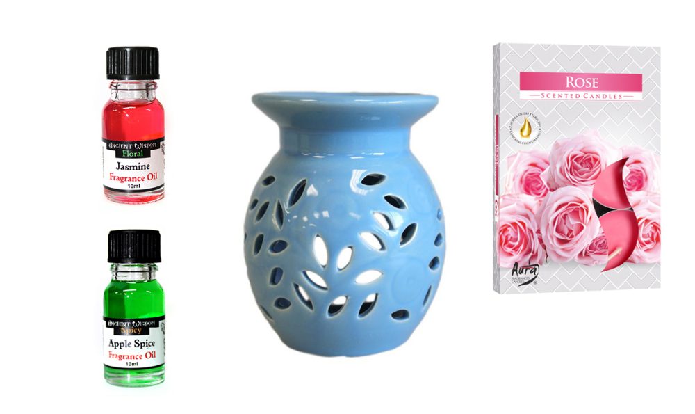 A blue ceramic oil burner with leaf cutouts sits beside two small bottles of fragrance oil and a box of rose-scented candles.