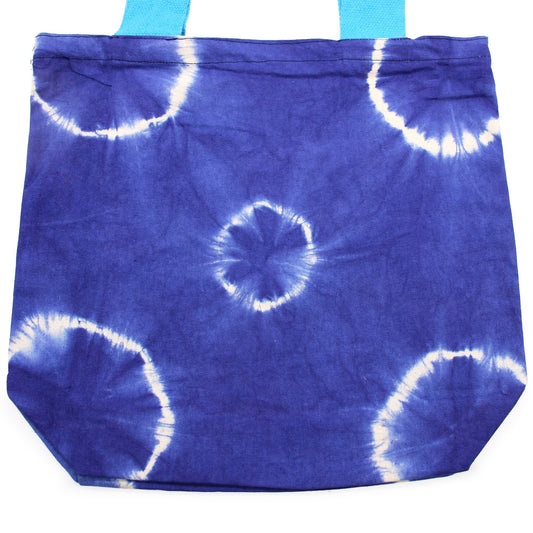 A blue tote bag with light-blue straps is shown. It has a tie-dye pattern, including a central flower-like design and partial rings. The background is a solid white.
