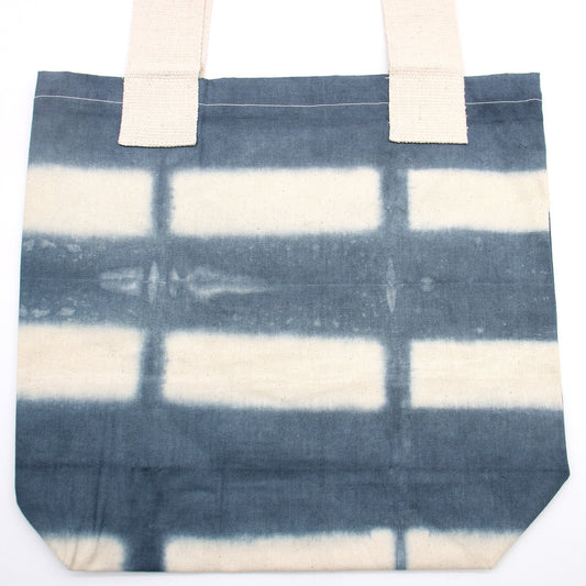 A canvas tote bag with white straps lies flat, displaying a blue and white grid pattern against a white background.