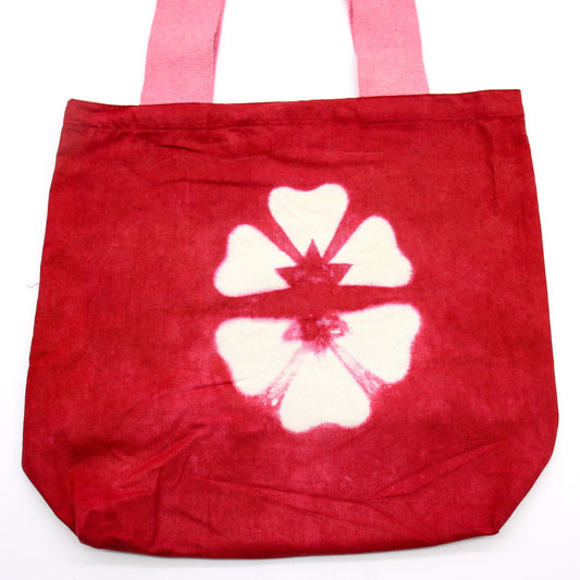 A red canvas tote bag displays a white flower design in its center, complete with two pink handles, resting on a white background.