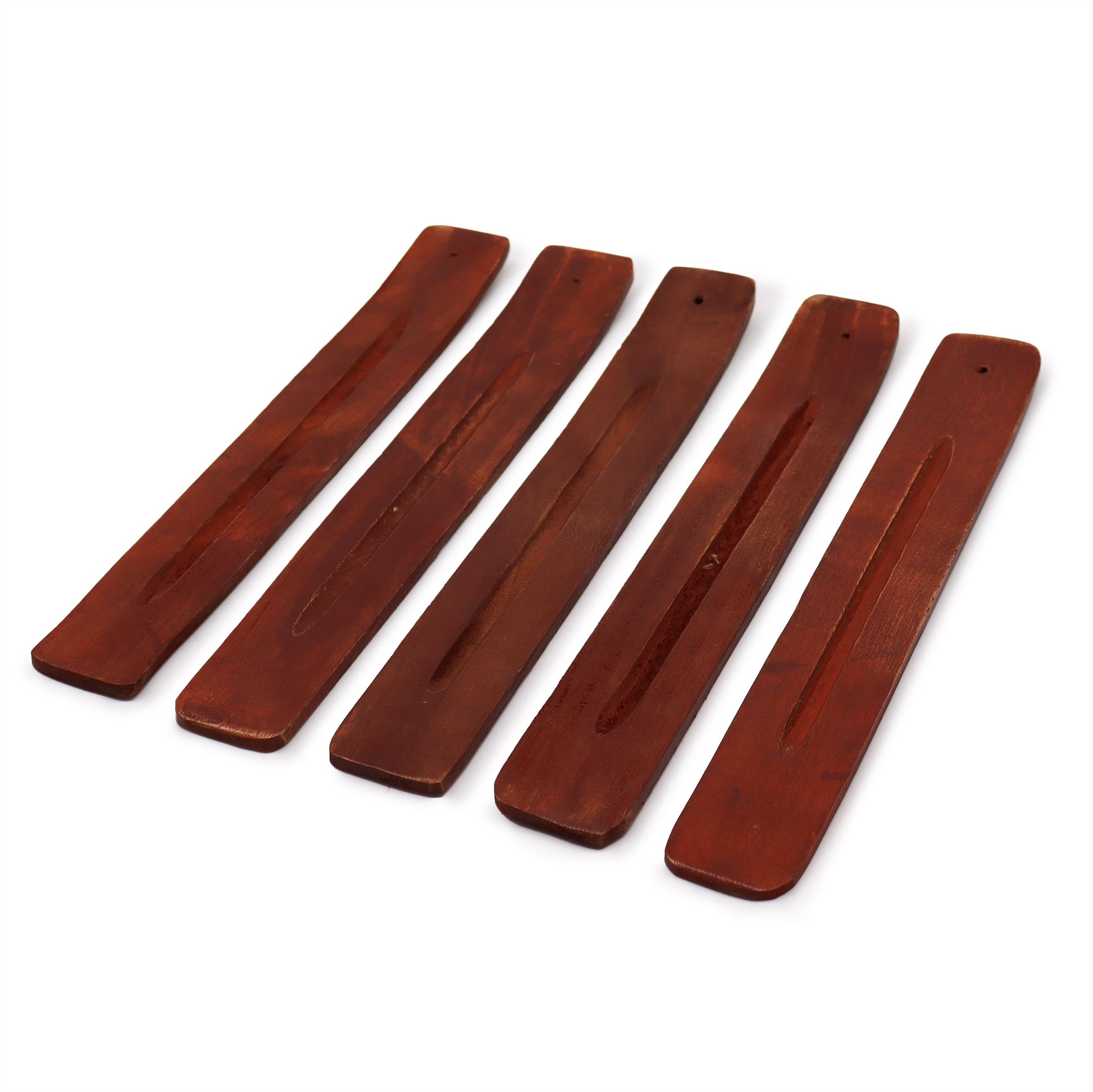 Wooden incense holders, elongated with a groove for sticks, are arranged side by side. They feature a reddish-brown finish and small holes at one end for the incense.