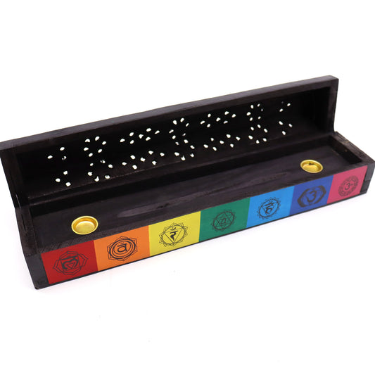 Wooden incense holder with a hinged lid, displaying chakra symbols in rainbow colors. Perforations on top distribute scent. Two round compartments hold incense cones or sticks in a minimal setting.