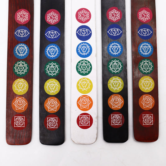 Five incense holders display colorful chakra symbols in columns. Each holder features red, orange, yellow, green, blue, and indigo motifs. The setup is on a plain white background.