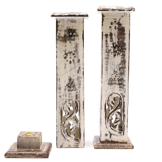 Two ornate candle holders with a distressed white finish, featuring cut-out patterns and decorative details, stand upright. A third, shorter piece lies flat nearby, all on a plain background.