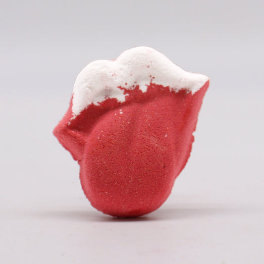A red, tongue-shaped bath bomb features a white frothy tip, standing upright against a plain gray background.