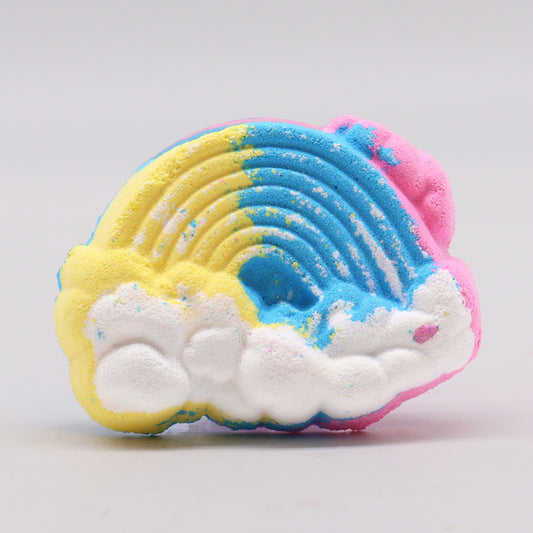 A colorful bath bomb shaped like a rainbow with distinct yellow, blue, and pink sections rests on a smooth, light surface, evoking a playful, vibrant atmosphere.