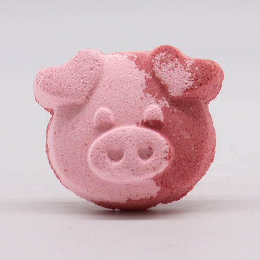 A pink bath bomb shaped like a pig's face rests on a flat surface, displaying a textured, dual-toned pattern against a neutral gray background.