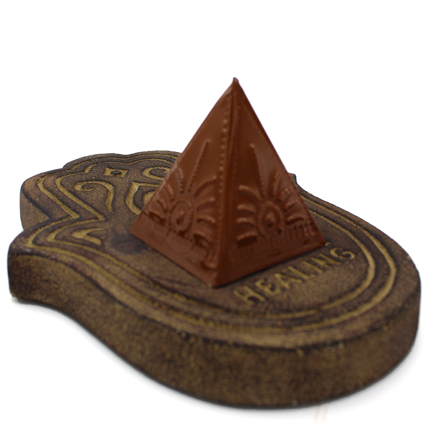 A brown pyramid rests on an intricately patterned, wooden base resembling a foot shape. The base features carved lines and the word "HEALING" inscribed near the pyramid.