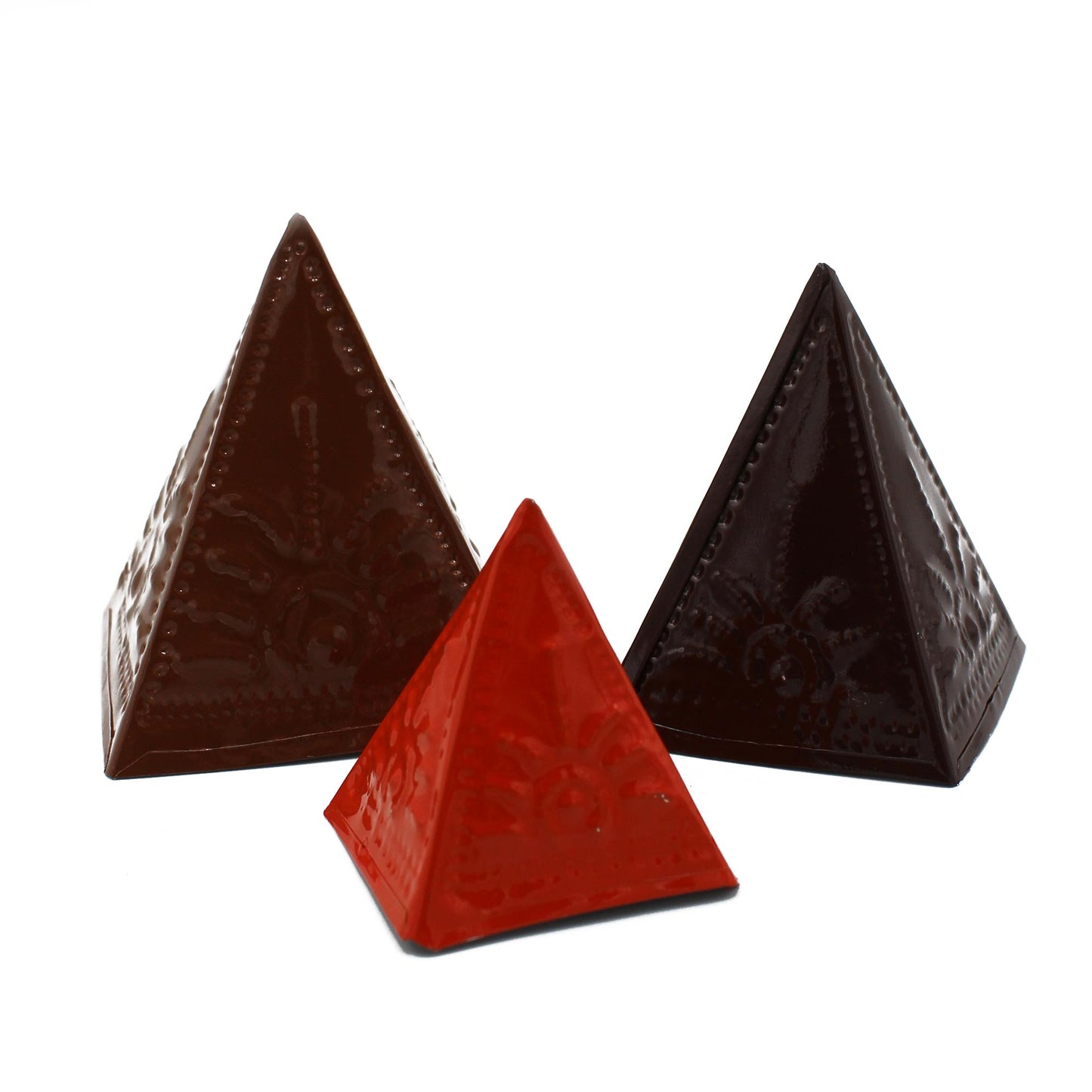 Three ornate chocolate pyramids are arranged side by side. The front pyramid is red, flanked by dark brown ones, all displaying embossed designs within a white background.