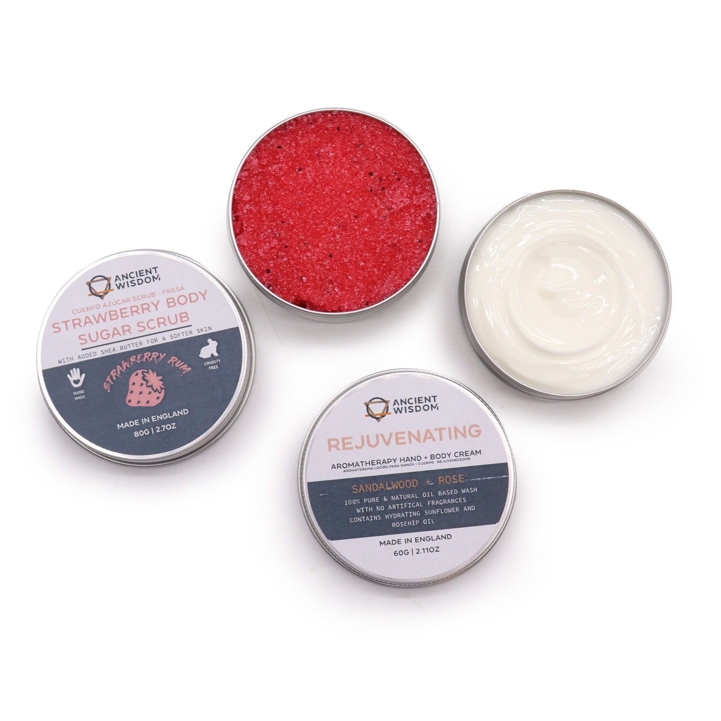Two small tins sit on a white background. One tin contains red strawberry body sugar scrub; the other holds a white hand and body cream. Both tins have labels detailing ingredients and origin ("Made in England").