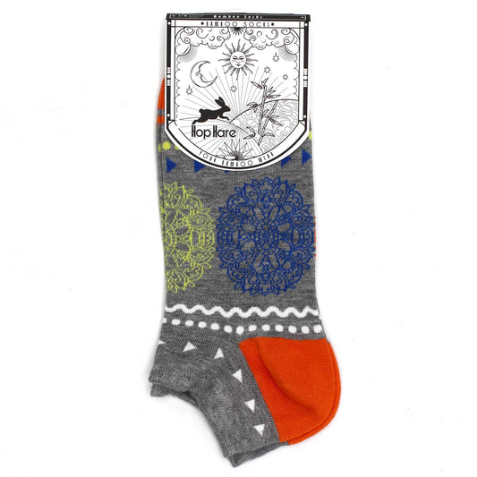 A pair of grey ankle socks, featuring blue and yellow circular patterns, is displayed against a white background. The socks have an orange heel and are packaged with a tag that reads: *BAMBOO SOCKS* Hop Hare YOUR BAMBOO WEAR. S/M.