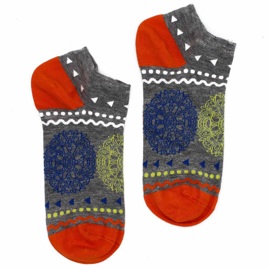 A pair of ankle socks lies on a white background. They are grey with orange toes and heels, and feature a patterned design of blue and green shapes.