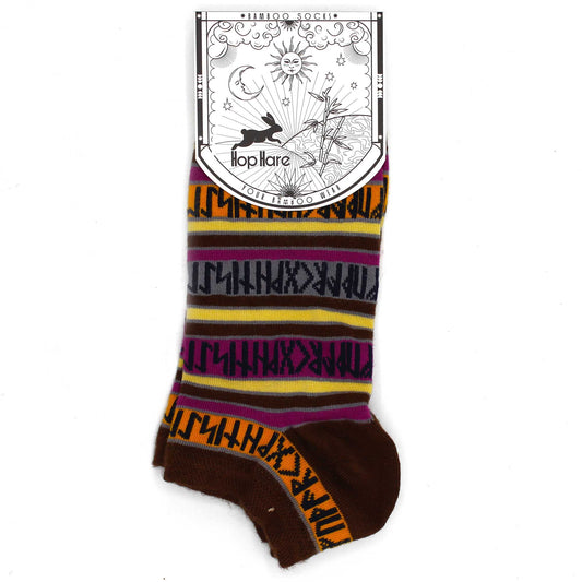 A brown sock with colorful horizontal stripes and dark symbols is displayed against a white background. The sock has a tag that reads: *BAMBOO SOCKS* Hop Hare YOUR BAMBOO WEAR.