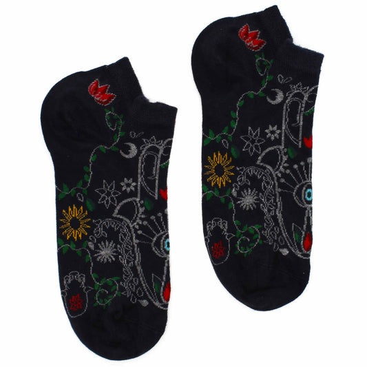 A pair of dark-blue ankle socks, patterned with stylized flowers, suns, and eyes, lies on a white background.