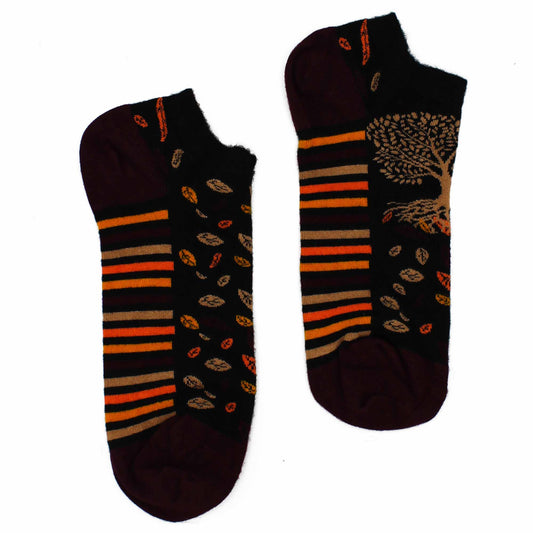 A pair of ankle socks lies on a white background. They are dark maroon and black with orange and tan stripes and a tree design. Scattered leaves are also visible on the socks.