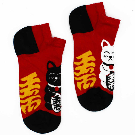A pair of red and black ankle socks, featuring Maneki-neko (beckoning cat) designs and Japanese characters, lies on a white background.