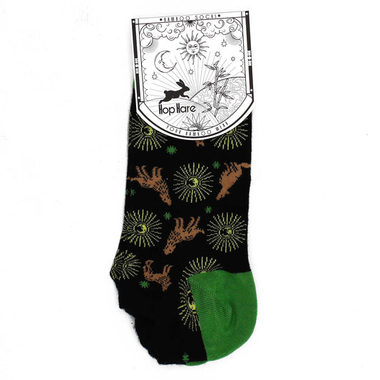 A pair of black bamboo socks, featuring a repeating pattern of rabbits and suns, displays a green heel and a label that reads "*BAMBOO SOCKS* Hop Hare YOUR BAMBOO WEAR".
