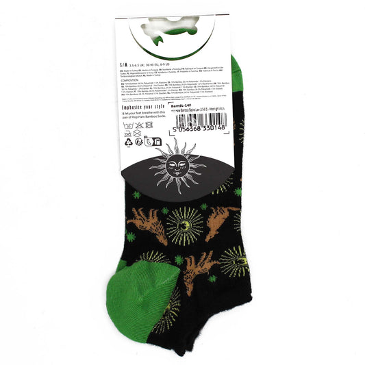 A pair of black ankle socks, adorned with a repeating pattern of suns and animals, is displayed on a white background; the socks feature a green cuff. The packaging includes size and composition details and a barcode: 5 056368 330148.