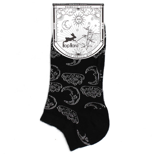 A black bamboo sock, displaying a moon and cloud pattern, rests on a white background; attached is a tag reading “Bamboo Socks,” “Hop Hare,” “Your Bamboo Wear,” and featuring a rabbit, sun, moon, and bamboo illustration.