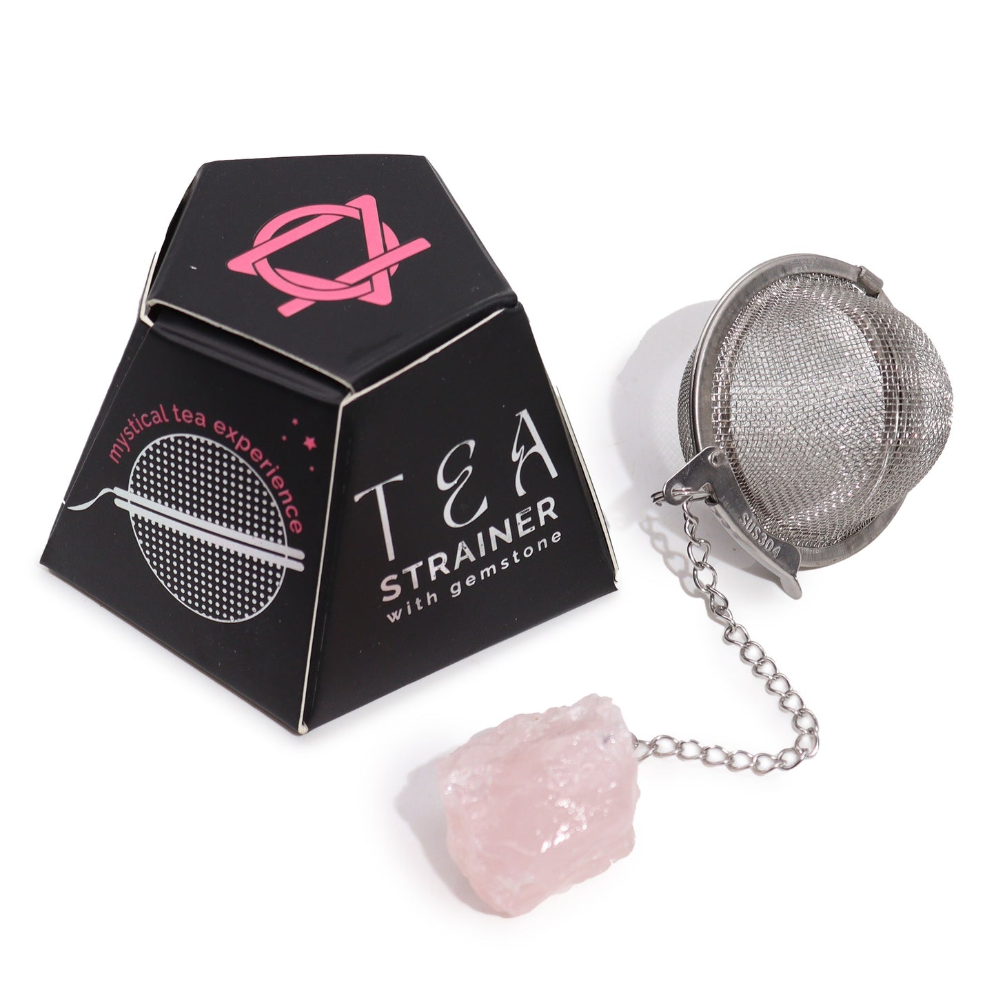 A metal tea strainer with a gemstone at the end of its chain lies next to black packaging labeled "TEA STRAINER with gemstone" and "mystical tea experience," featuring a pink design.