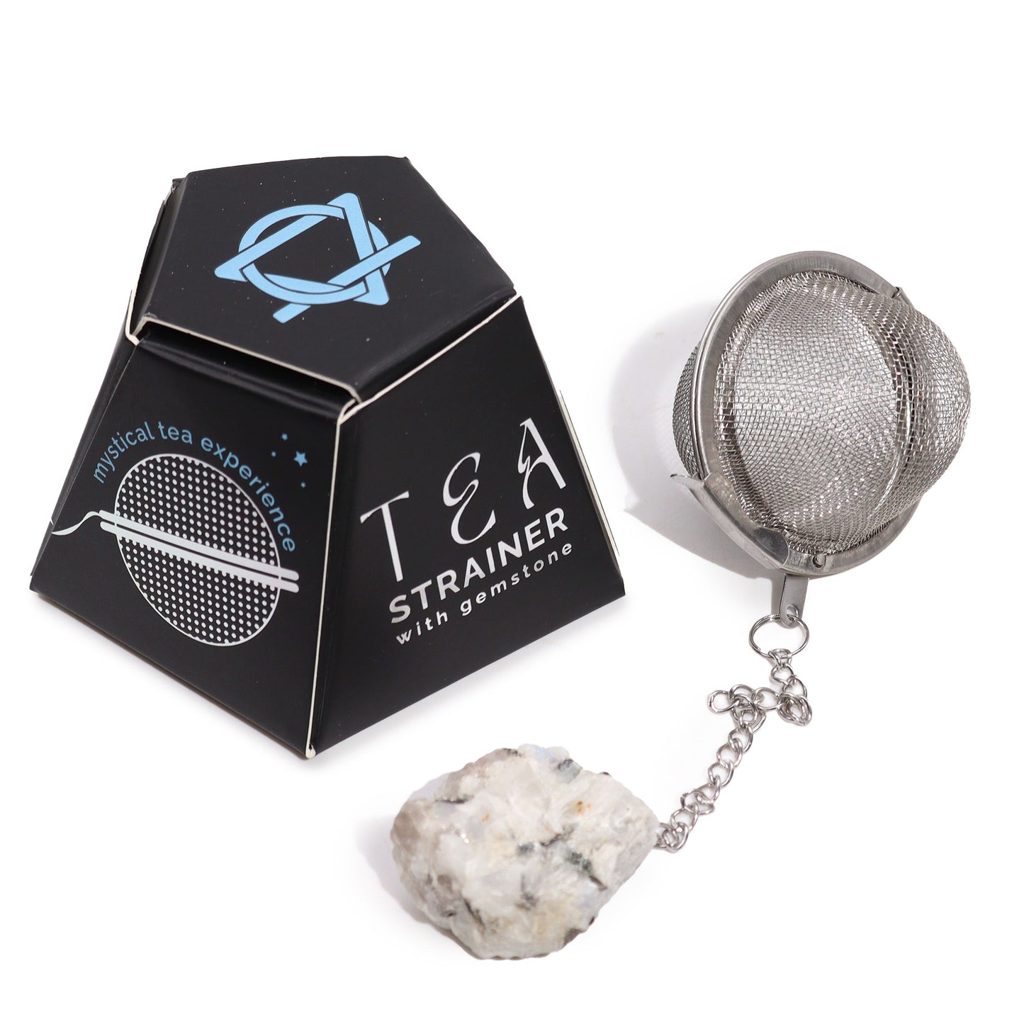 A metal tea strainer with a chain ending in a gemstone rests next to a black hexagonal box labeled "mystical tea experience" and "TEA STRAINER with gemstone."