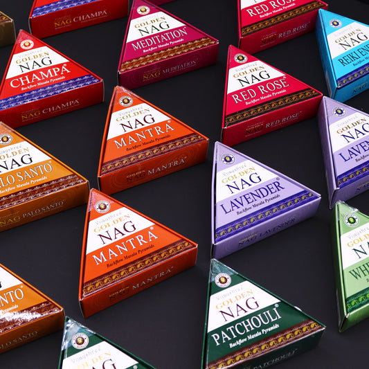 Triangular incense boxes labeled "Golden Nag" display various scents like Champa, Meditation, Mantra, Red Rose, Palo Santo, Lavender, and Patchouli on a black background, arranged neatly.