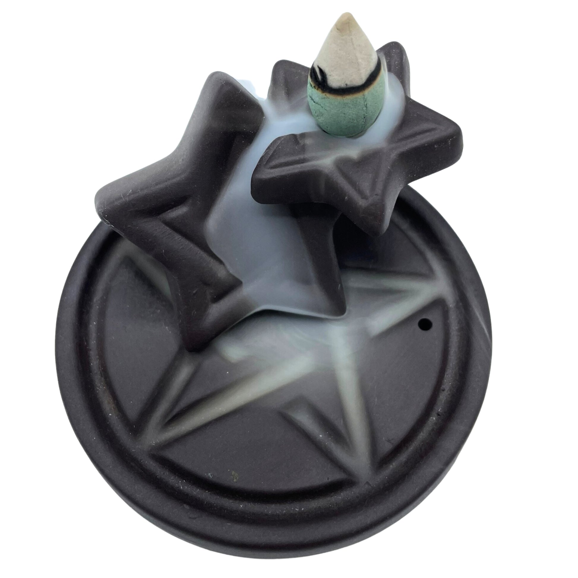 A dark star-shaped incense holder releases smoke that flows over its surface, set on a round base with a star imprint, against a plain white background.