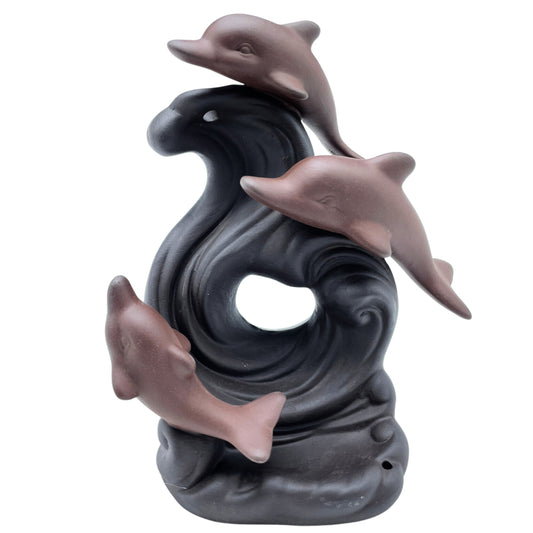 A sculpture of three dolphins made of a reddish material appears to leap over a stylized, swirling black wave, set against a plain white backdrop.
