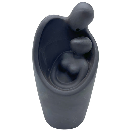 A smooth, abstract sculpture depicts two figures embracing, with one cradling the other, set against a plain white background.