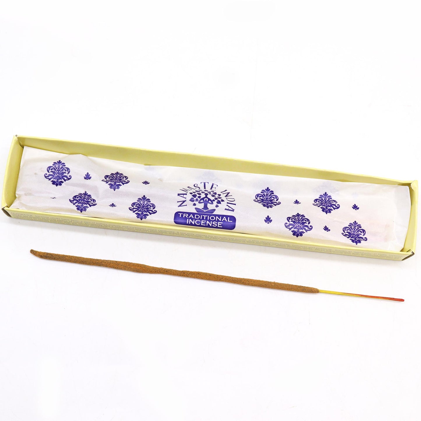 Incense stick lies beside an open box labeled "Namaste India Traditional Incense" with purple decorative patterns, placed on a plain white background.