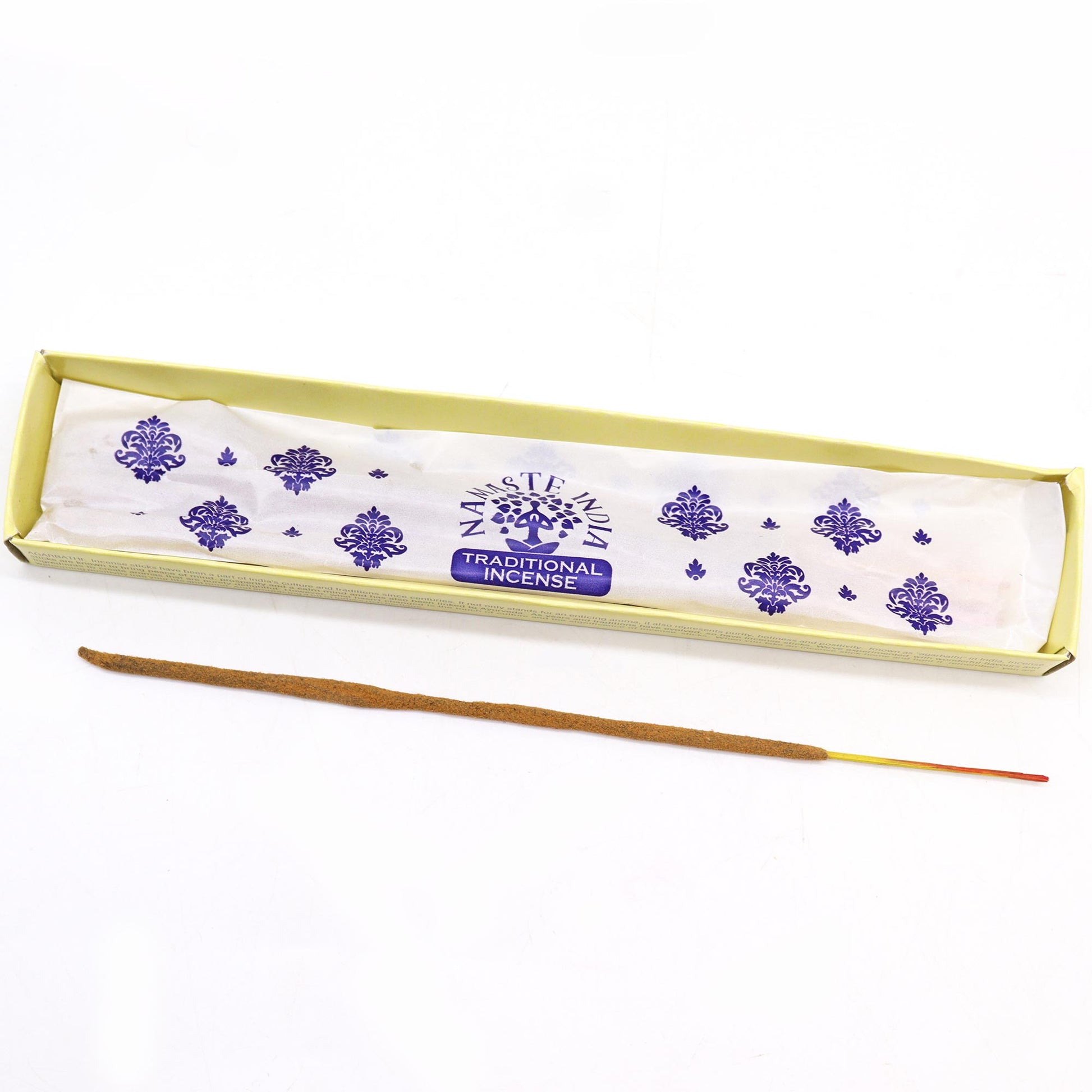 Incense stick lies next to an open box labeled “NAMASTE INDIA TRADITIONAL INCENSE,” featuring purple decorative patterns on white paper, set against a plain white background.