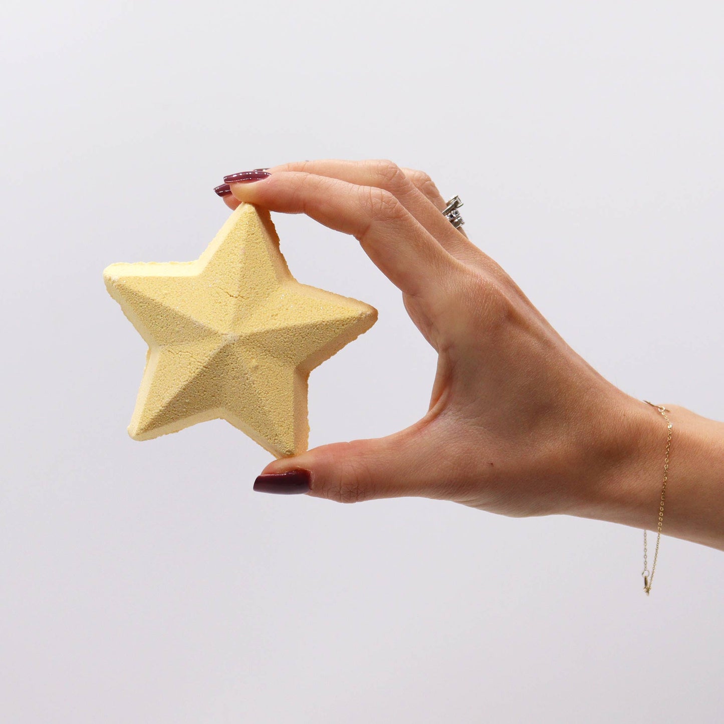 A hand with dark red nails holds a textured, yellow star-shaped object against a plain white background.