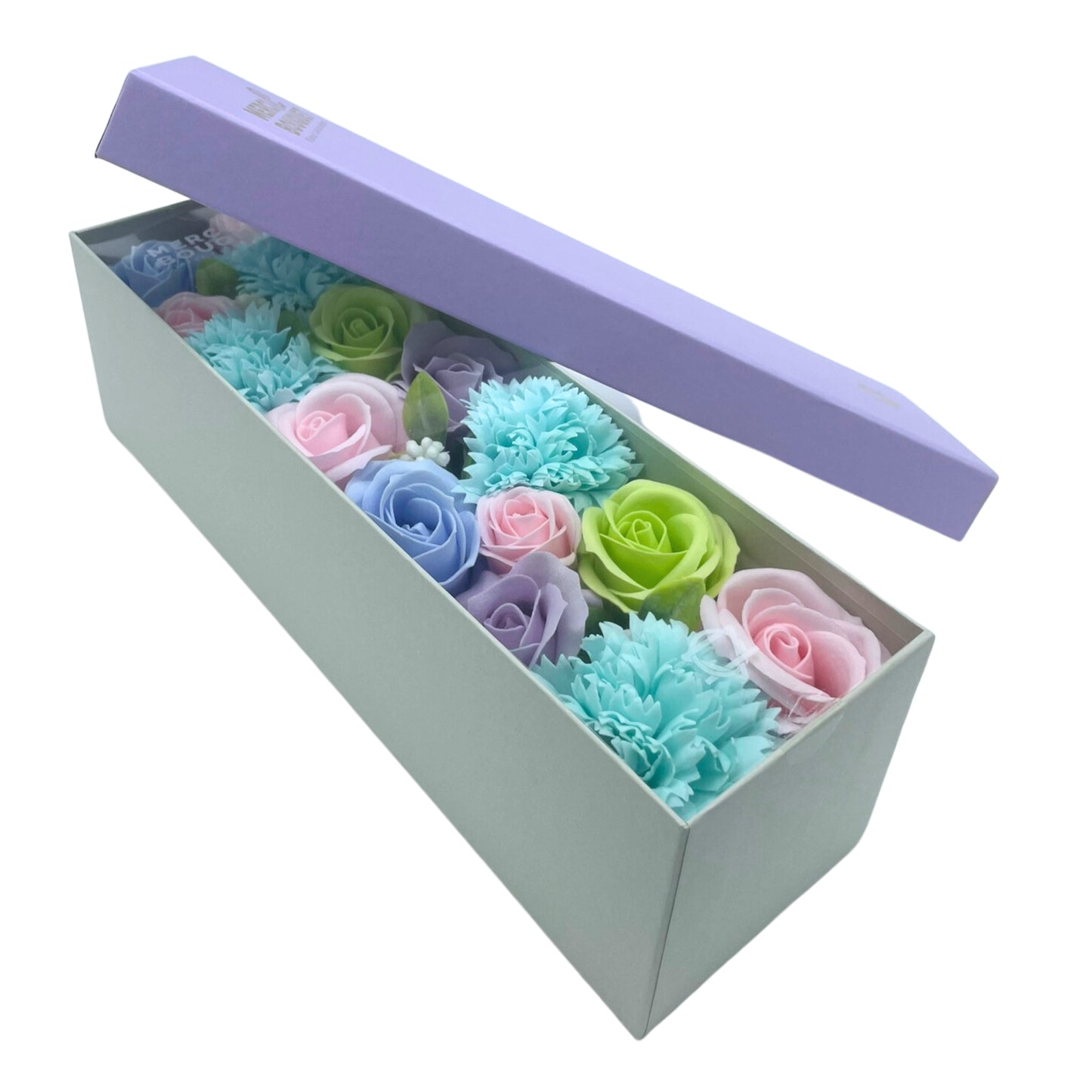 A light-green box contains pastel soap flowers; its lavender lid is ajar. The arrangement includes roses and carnations.