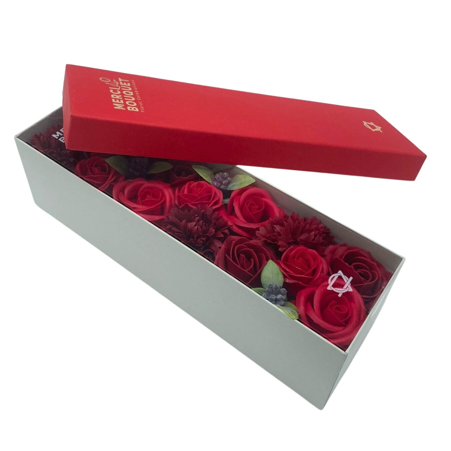 A light-grey box containing a red soap flower bouquet sits atop a red lidded box. The red box reads: MERCI BOUQUET Floral Creations.