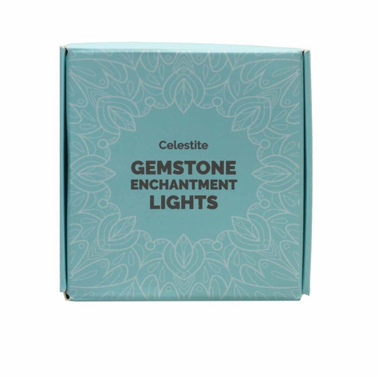 A light blue square box reads "Celestite GEMSTONE ENCHANTMENT LIGHTS," surrounded by a white floral pattern. The box sits against a plain white backdrop.