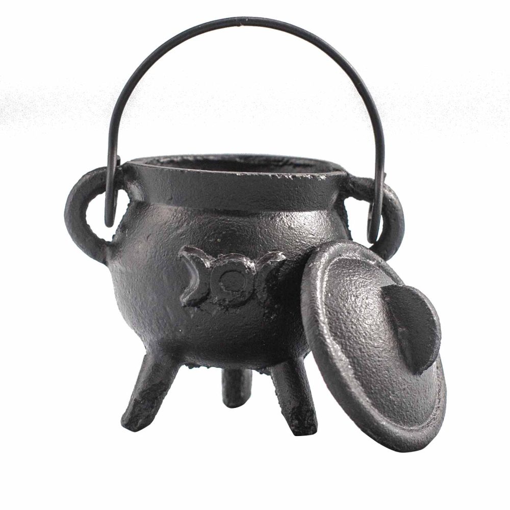 A small black cast-iron cauldron stands with its lid partially off, featuring a decorative design on its side. It has a handle and three legs, set against a plain background.