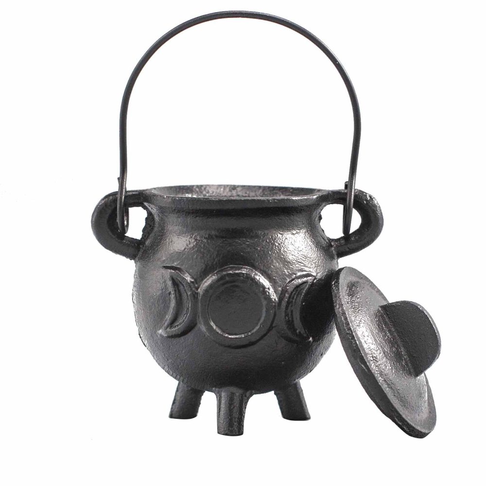 A small black cauldron rests with its lid slightly ajar, displaying a design of triple moons on its surface. It has a handle and stands on three short legs.