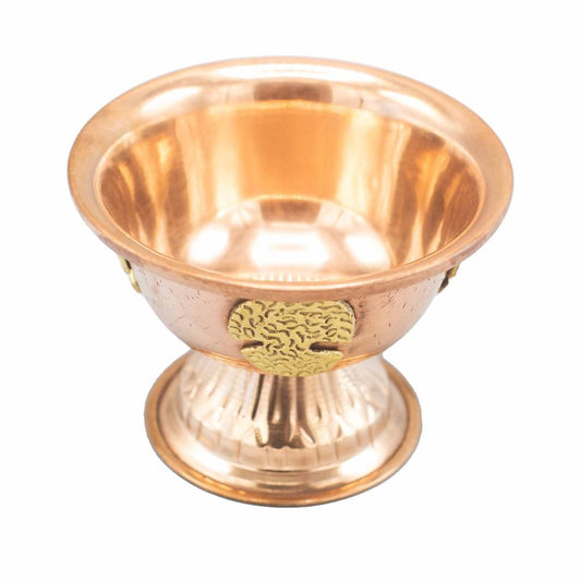 A polished brass chalice with intricate golden embellishments rests on a textured circular base, reflecting light in a bright, neutral space.
