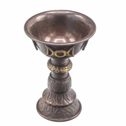 A bronze chalice with ornate gold patterns sits atop a decorative base, featuring intricate designs and markings, set against a plain white background.