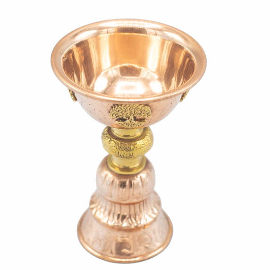 A polished, ornate copper chalice with a decorative gold section on the stem sits against a plain white background, showcasing intricate embossed designs.