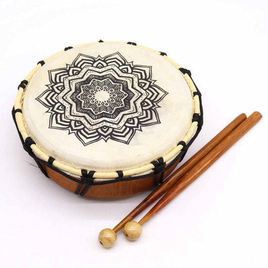 A hand drum with a black geometric pattern is placed alongside two wooden mallets. The scene is set against a plain white background.