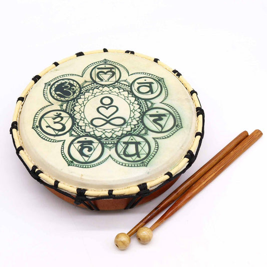 A hand drum with chakra symbols printed on its surface lies on a white background, accompanied by two wooden mallets.