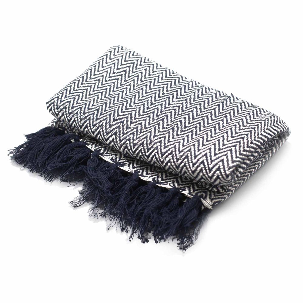 A navy and white chevron patterned throw blanket rests on a white background; its folded edges display a dark fringe.